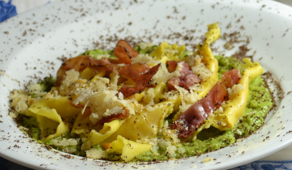 Tortelli di zucca su letto di purea di piselli conditi con prosciutto crudo croccante e briciole di Parmigiano Reggiano abbrustolite .
